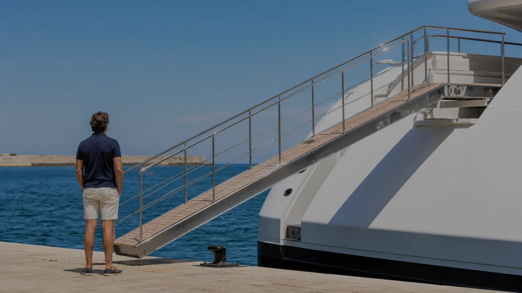 Passerella di poppa che sale dalla banchina al ponte di uno yacht, con una persona accanto per dare la scala